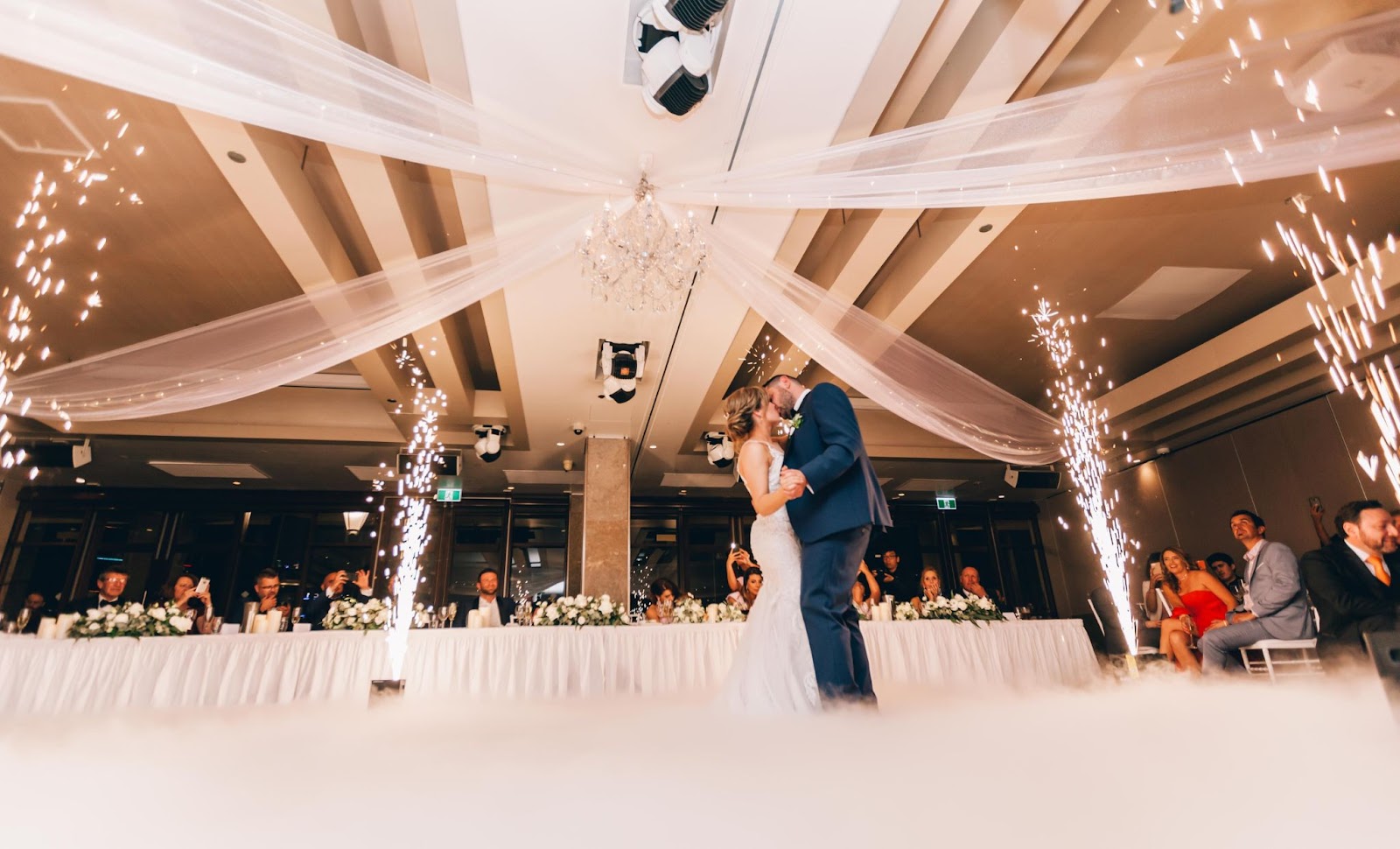 couple kissing during their first dance as sparklers go off on each corner of the wedding dance floor